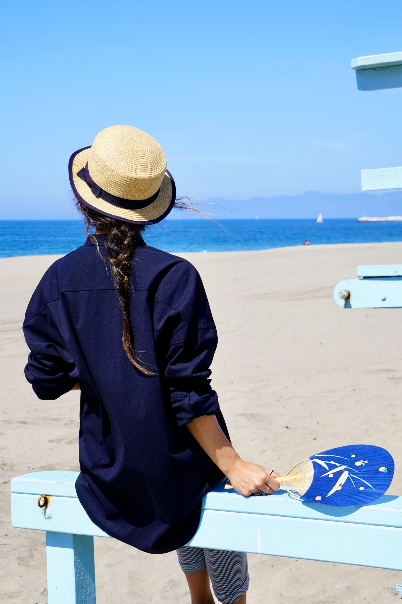 ベンチに座り、うちわを持って海を眺める女性